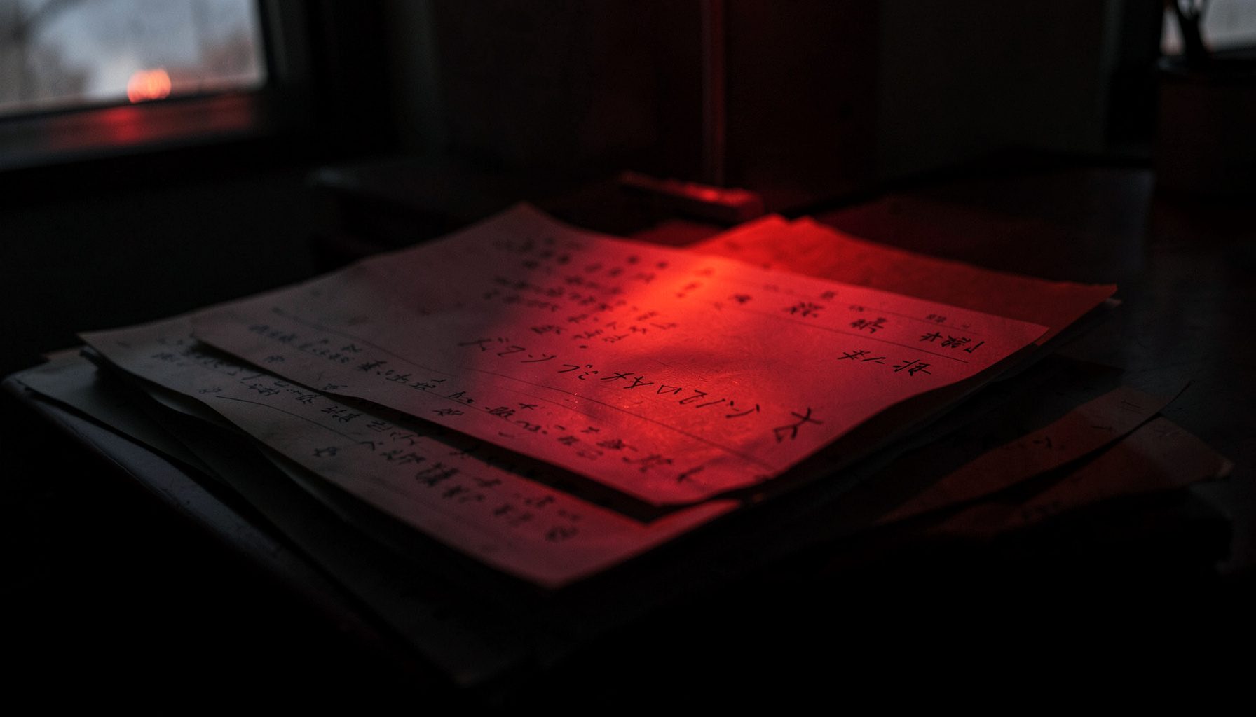 カウンターに積まれた紙の伝票と古い手書きメモ。窓から差し込む夕日が赤い色を帯びた書類に反射し、静かな事務所の雰囲気の写真